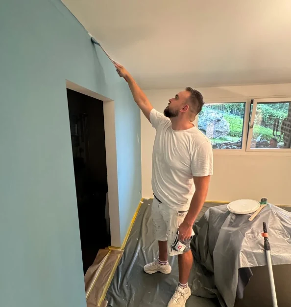 Florian Sapulovic streicht eine Wand, Boden und Möbel sind abgedeckt